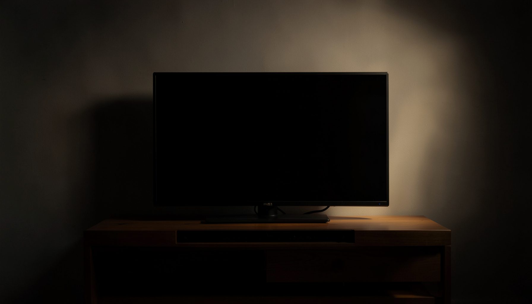 A dark flat-screen television glowing with warm light on a wooden media console in a dim room, calm and cinematic mood